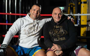 Two of the stars of the film "Kaikohe Blood & Fire" are sat on the edge of a boxing ring and looking at the camera.