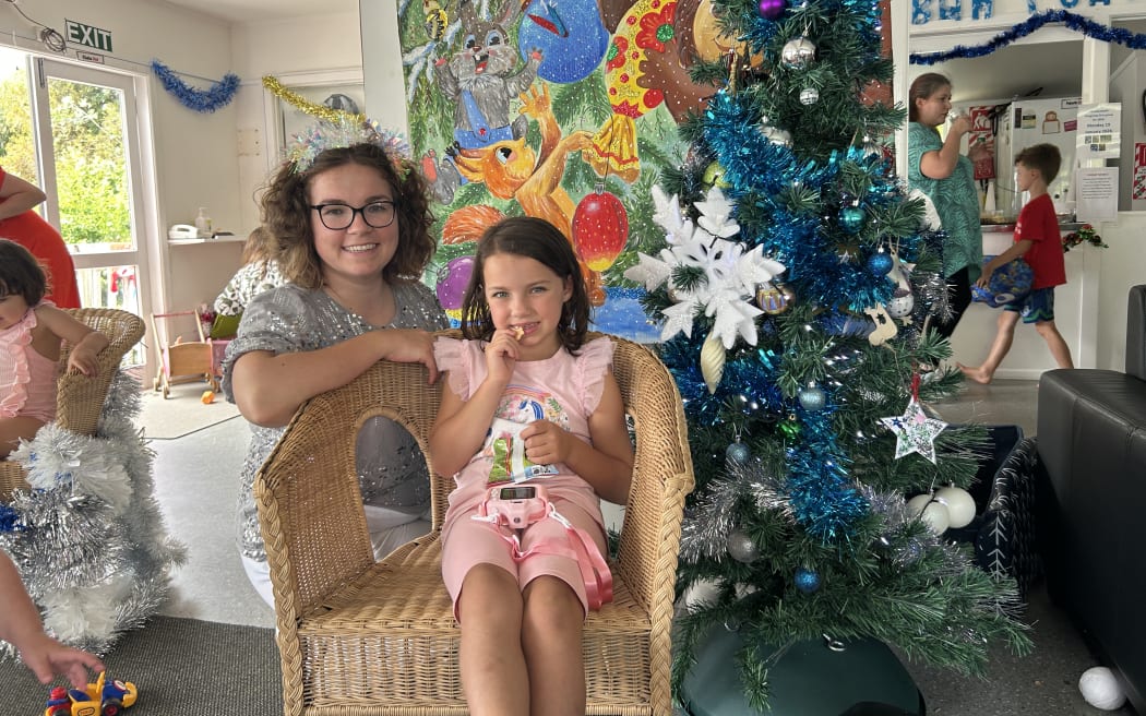 Picture of a woman and a young girl dressed in festive outfit, they are pictured next to a Christmas tree.
