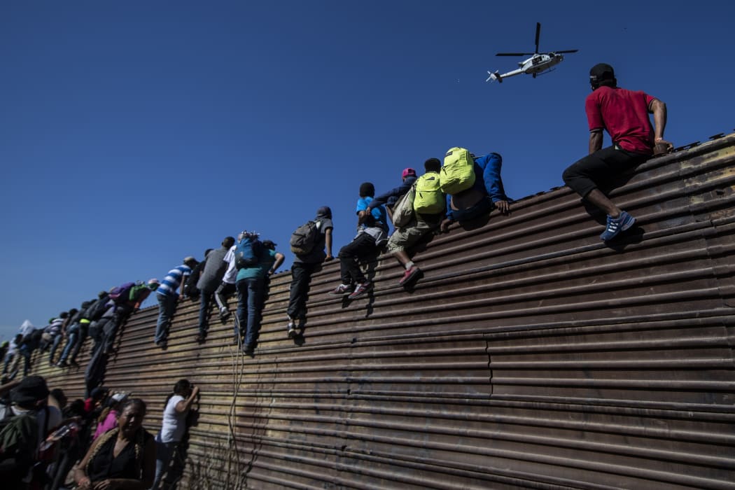 A group of Central American migrants climb a metal barrier on the Mexico-US border.