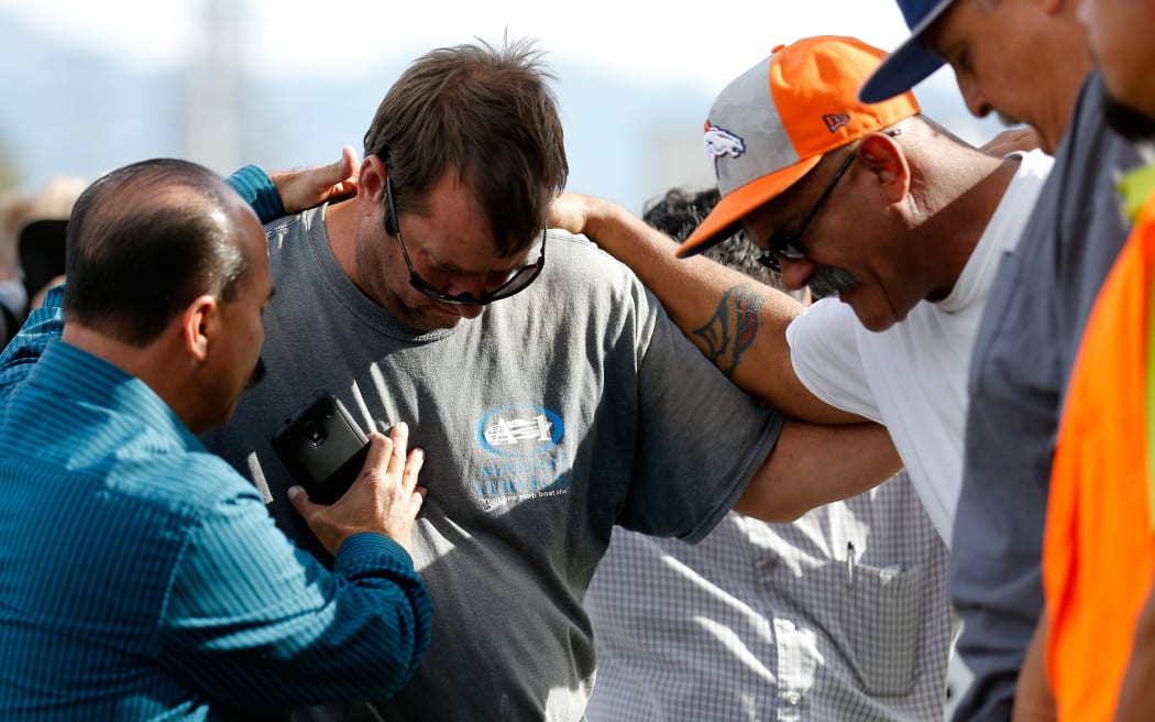 A group of men embrace in prayer outside the crime scene where the suspects in the shooting at the Inland Resource Center were killed.