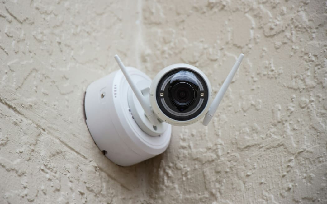 A security camera, high on the wall of a building.