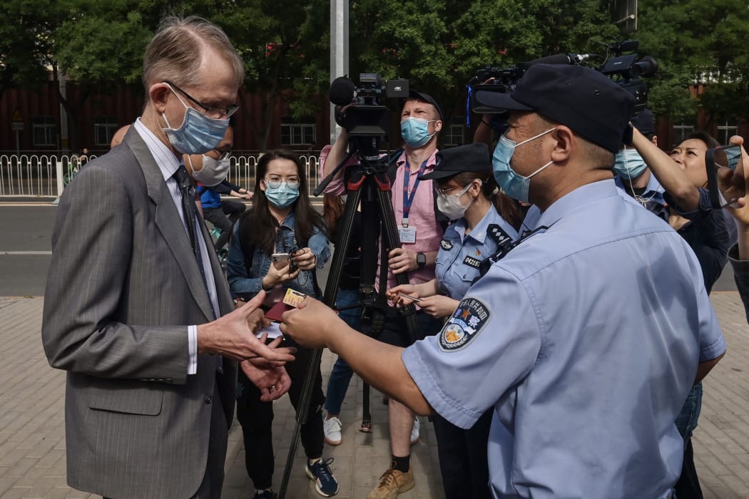 A Chinese police officer returns an ID card to Australian Ambassador to China Graham Fletcher (left) as he arrives at the Beijing Second Intermediate People's Court before the trial of Australian academic Yang Hengjun on May 27, 2021.