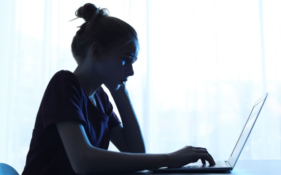 Upset teenage girl with laptop at table indoors. Danger of internet
