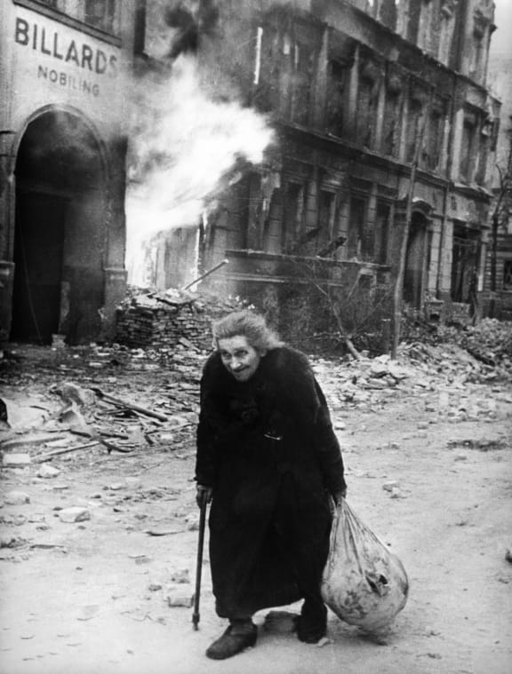 A photo taken in 1945 in Berlin shows an old woman walking on a street where buildings are burning during the Allied bombings at the end of World War II.