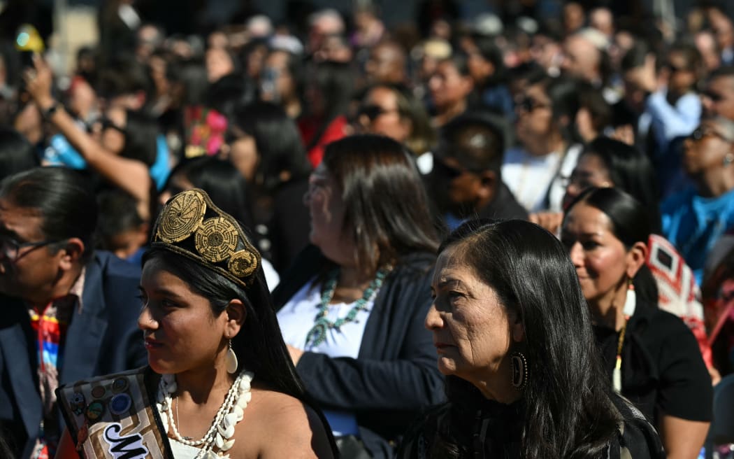 US Interior Secretary Deb Haaland (R) listens to US President Joe Biden speak at the Gila River Crossing School in the Gila River Indian Community, in Laveen Village, near Phoenix, Arizona on October 25, 2024. - Biden apologized for one of the country's "darkest chapters:" the abduction of Native American children from their families and placement in abusive boarding schools aimed at erasing their culture. The first public apology issued by a sitting US president. From the early 1800s until the 1970s, the US ran hundreds of Indian boarding schools across the country to forcibly assimilate Native children into European settler culture, including conversion to Christianity. (Photo by ANDREW CABALLERO-REYNOLDS / AFP)