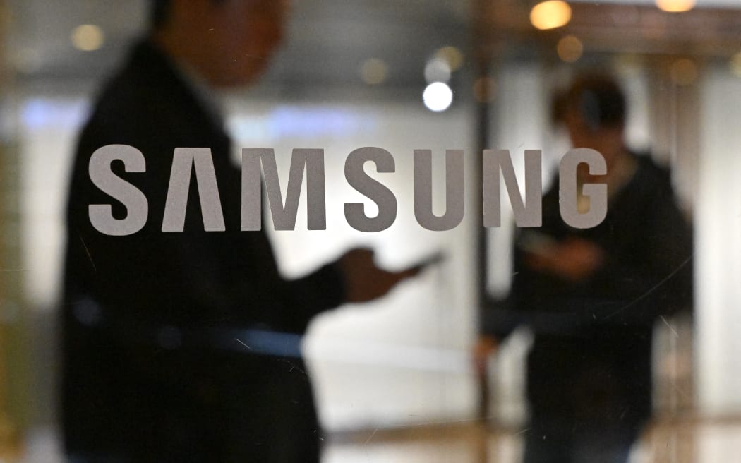 People walk past the Samsung logo displayed on a glass door at the company's Seocho building in Seoul on April 5, 2024. Samsung Electronics said on April 5, it expects first-quarter operating profits to rise more than 10-fold year on year as chip prices recover. (Photo by Jung Yeon-je / AFP)