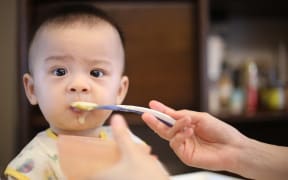 A baby being spoon fed solid food.