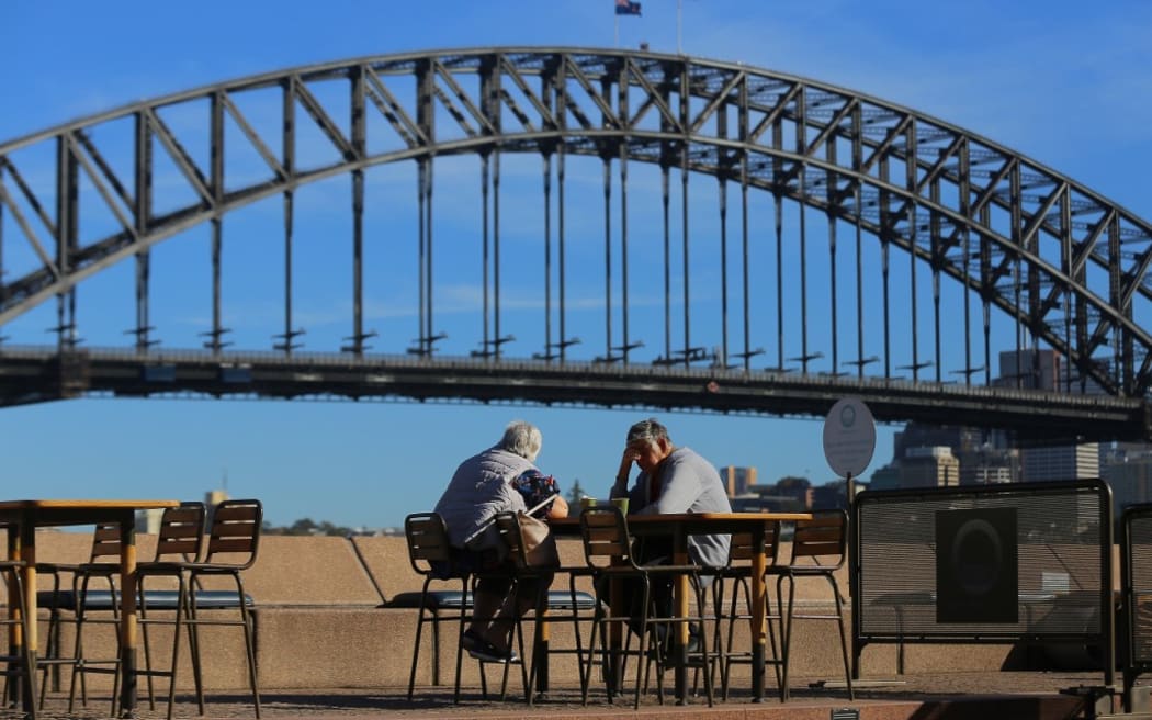 SYDNEY, AUSTRALIA - MARCH 19: An elderly couple sit at a table in front of the Sydney Harbour Bridge, following an outbreak of coronavirus (COVID-19), in Sydney, Australia.
