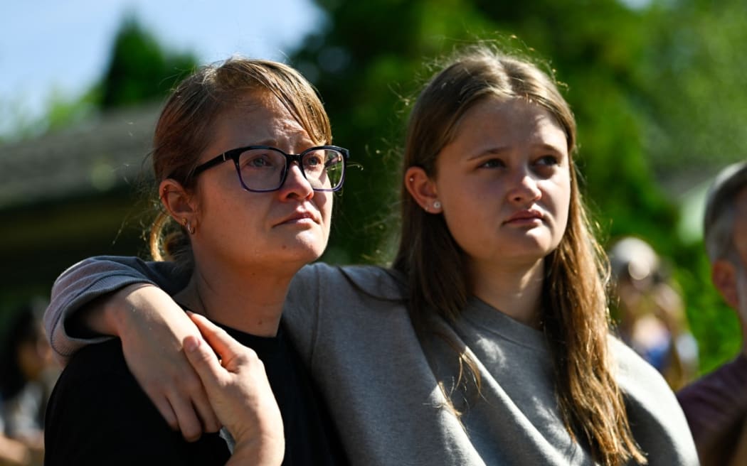 Renee Landers (L) and Norah Landers (R) listen as Minneapolis Mayor Jacob Frey speaks following a mass shooting at Annunciation Catholic Church on August 27, 2025 in Minneapolis, Minnesota. According to Minneapolis Police, a gunman fired through the windows of the church at worshippers sitting in pews during a Catholic school Mass, killing two children and injuring at least 17 others. The gunman reportedly died at the scene from a self-inflicted gunshot wound.   Stephen Maturen/Getty Images/AFP (Photo by Stephen Maturen / GETTY IMAGES NORTH AMERICA / Getty Images via AFP)