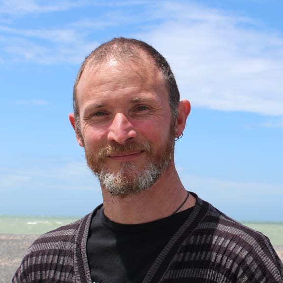 Composer Phil Brownlee stands with his back to the sea.