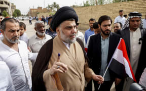 Iraqi Shiite cleric and leader Moqtada al-Sadr (C-L) shows his ink-stained index finger and holds a national flag while surrounded by people outside a polling station in the central holy city of Najaf on May 12, 2018