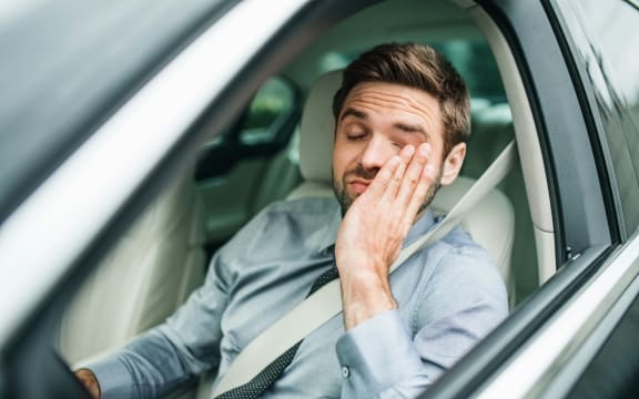 Man rubs his eyes at the wheel of a car