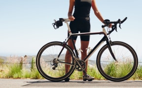 Low section shot of female athlete standing with her bicycle. Woman cyclist with her bike on country road. Cropped shot of female triathlete with her cycle.