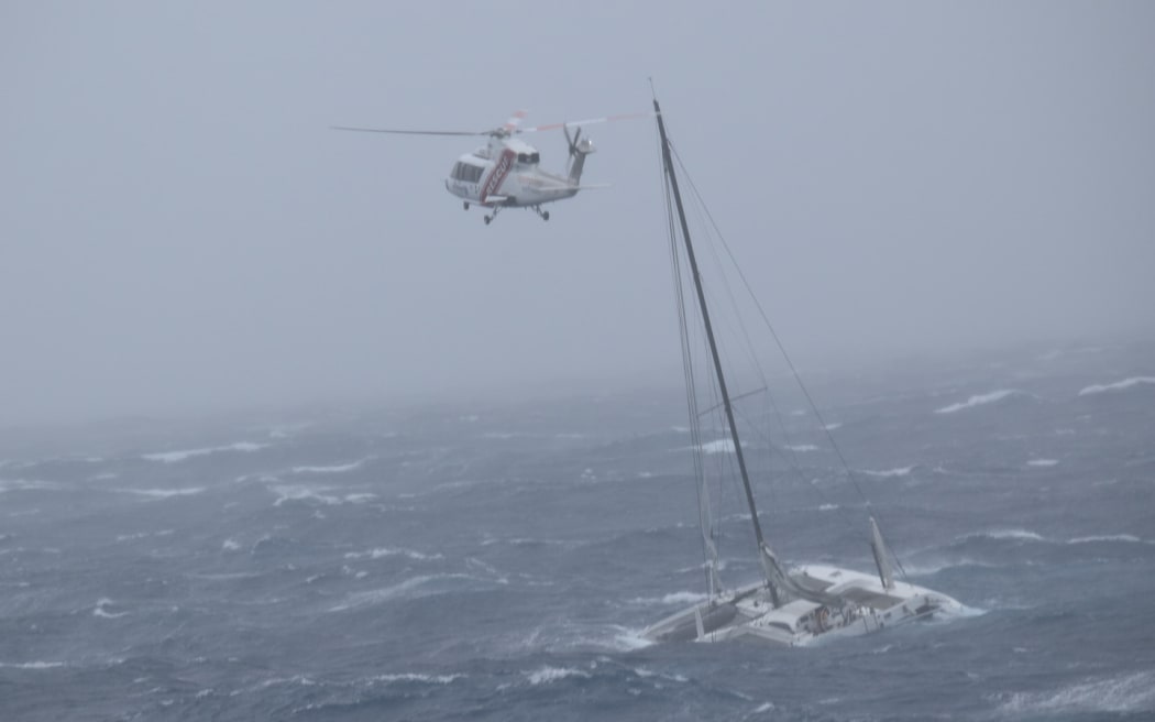 A catamaran that drifted out to sea in strong winds can be seen in the water with a helicopter flying above.