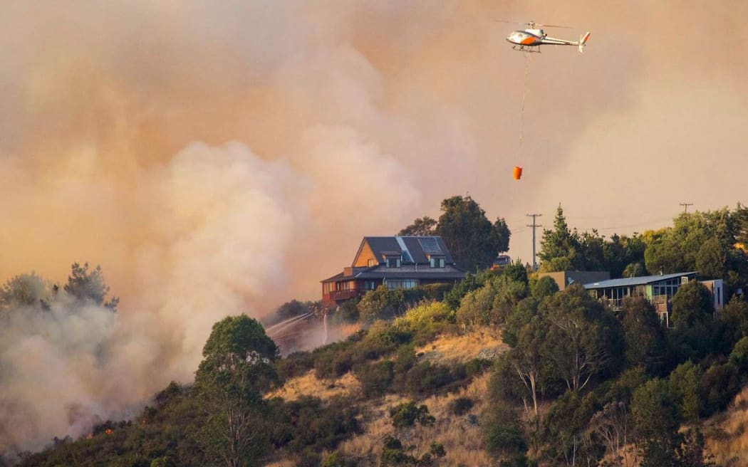 Firefighters try to save a house from fire on Port Hills in Christchurch. The fires destroyed nine houses and one helicopter pilot died fighting the blaze.