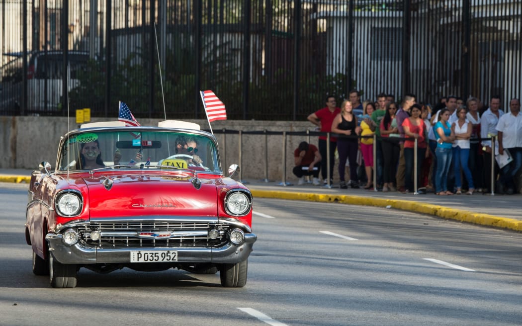 A vintage car with US flags drives by the US embassy in Havana as the countries formally resume diplomatic relations.