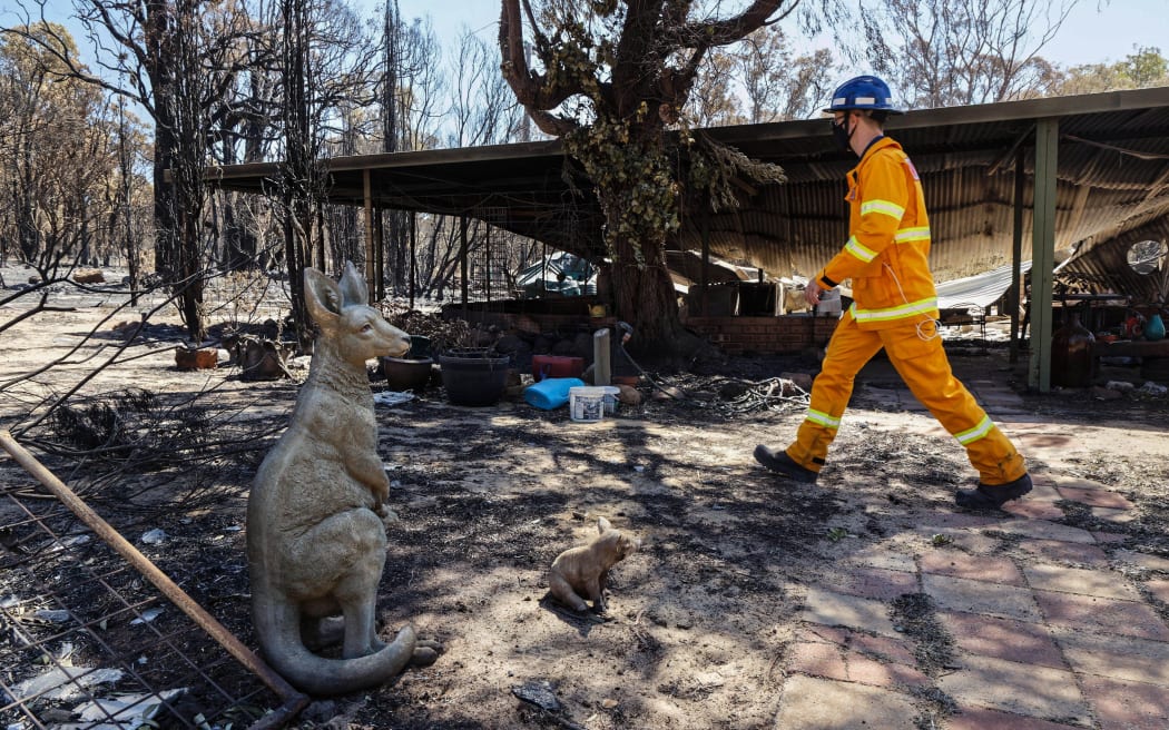 A man  walks past an ornamental statue of a kangaroo in the yard of a razed house after bushfires in Gidgegannup, some 40 kilometres north-east of Perth on February 4, 2021.