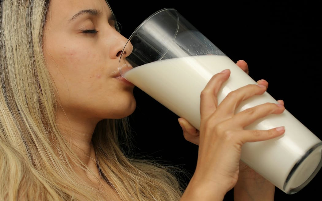 A blonde woman drinking a large glass of milk