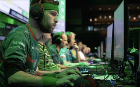 A line-up of men wear headphones and stare intently at individual screens.