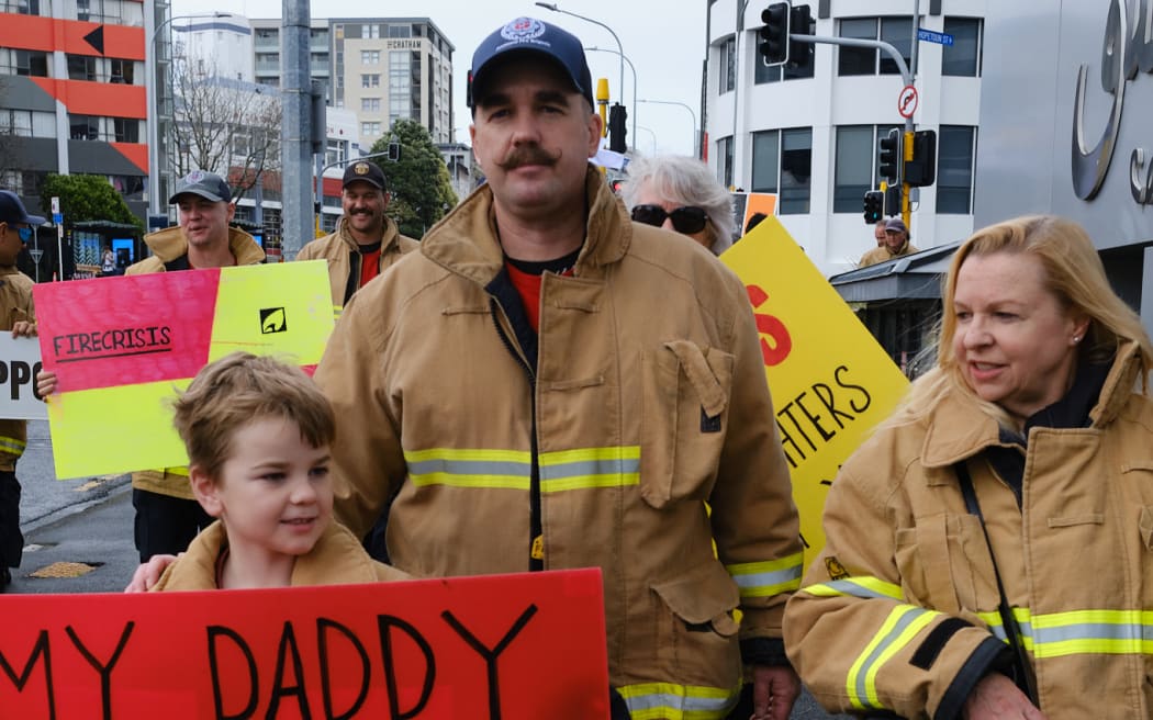 A boy holds a sign reading "My daddy has to work too much" at the Auckland Central firefighters strike on 26 August 2022.