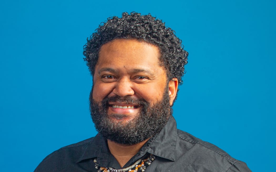 Koroi smiling wearing a dark shirt and necklace.