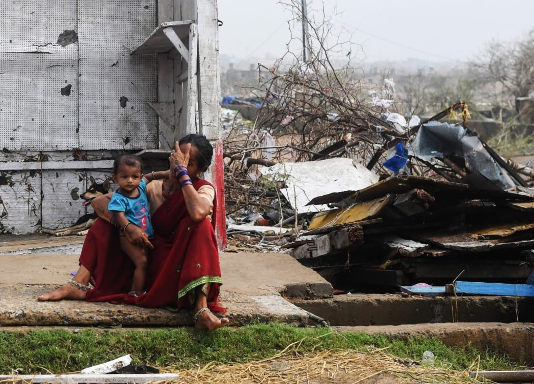 An Indian woman sits with her child next to storm-damaged buildings in Puri in the eastern Indian state of Odisha,