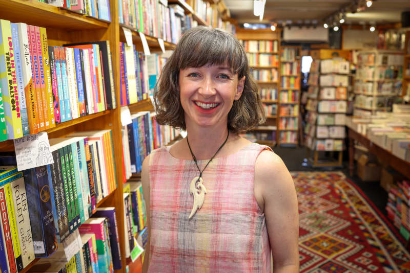 Jenna Todd is standing in the Mt Eden bookshop Time Out. She is surrounded by bookshelves.