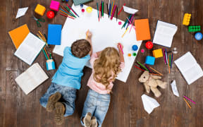 Happy children. Top view creative photo of little boy and girl on vintage brown wooden floor. Children lying near books and toys, and painting