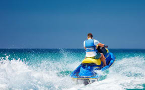 young adult man running the wave on jet ski during summer vacation