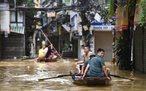 People wade through flood waters on a boat in Hanoi on September 12, 2024, as heavy rains in the aftermath of Typhoon Yagi brought flooding to northern Vietnam. The number of people killed after Typhoon Yagi swept through northern Vietnam bringing flash floods and landslides has risen to 197, the government said on September 12. (Photo by NHAC NGUYEN / AFP)