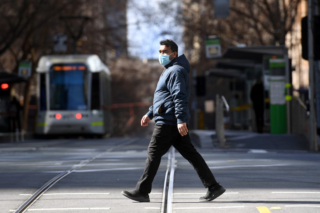 A man crosses an empty street in Melbourne on 23 August 2021, as the city experiences its sixth lockdown while battling an outbreak of the Delta variant of coronavirus.