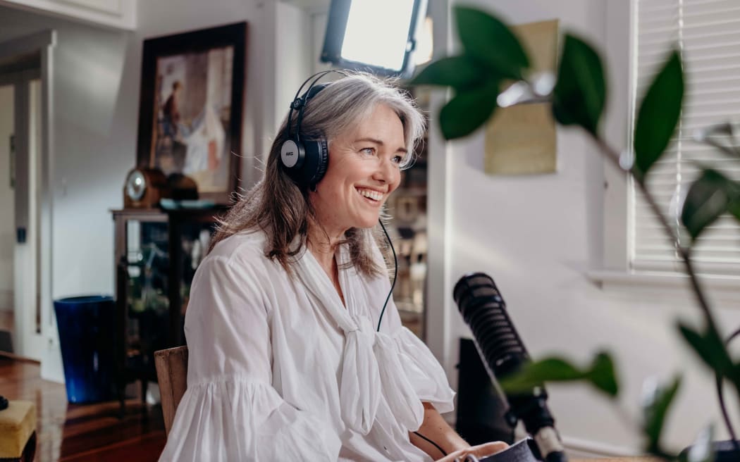 Petra sits at a desk with headphones on, speaking into a microphone and smiling.