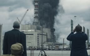 Comrades Legasov and Schcherbina watch as helicopters drop sand and boron on reactor four.
