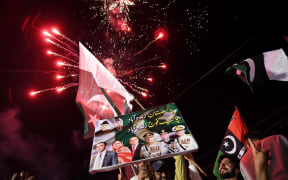 Pakistan Peoples Party (PPP) activists hold placards and wave Pakistani national flags as fireworks explode during a march expressing solidarity with the country's armed forces as they celebrate after a ceasefire between Pakistan and India, in Larkana, Sindh province on May 11, 2025. A ceasefire appeared to hold on May 11, 2025, between India and Pakistan, hours after the nuclear-armed rivals accused each other of violating a truce that brought them back from the brink of all-out war. The ceasefire was agreed on May 10, 2025, after four days of missile, drone and artillery attacks which killed at least 60 people and sent thousands fleeing, in the worst violence since India and Pakistan's last open conflict in 1999. (Photo by Ahmed Raza SOOMRO / AFP)