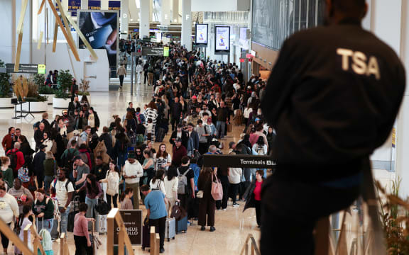 A Transportation Security Administration (TSA) agent looks on passengers queue to go through security at New York's LaGuardia airport on March 22, 2026. Immigration agents will be deployed in US airports beginning March 23, aiming to alleviate soaring congestion at security screenings amid a weeks-long budget standoff over President Donald Trump's mass deportation drive, officials said. Trump announced the extraordinary move in a social media post Sunday morning, sending officials racing to quickly develop a plan. (Photo by CHARLY TRIBALLEAU / AFP)