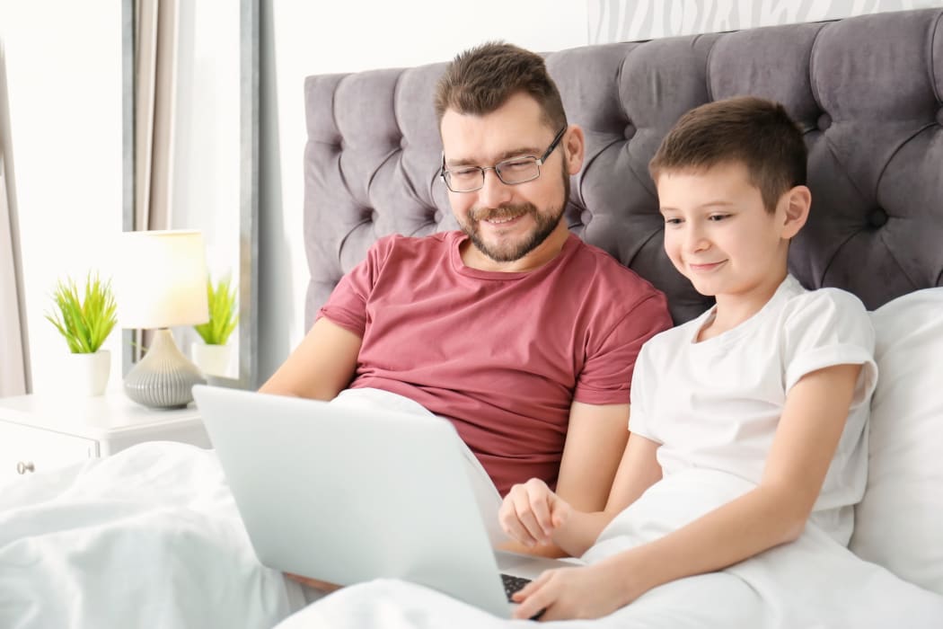 Little boy and his dad using laptop in bedroom
