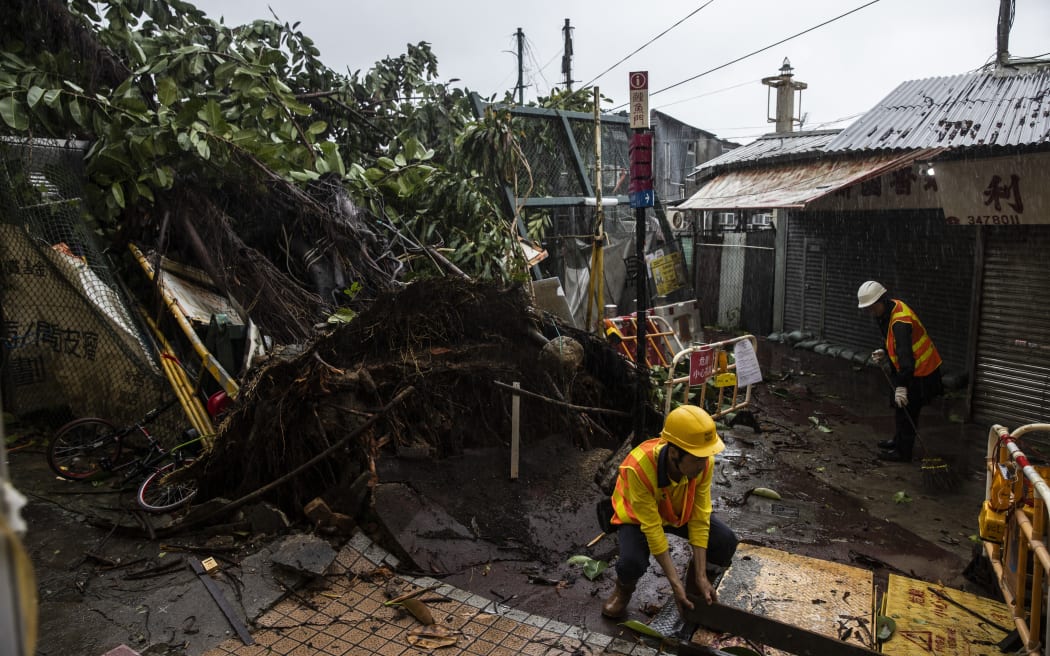 Workers clean up around a fallen tree caused by Typhoon Saola in a village in Lei Yue Mun in Hong Kong on 2 September, 2023. Typhoon Saola swept across southern China on 2 September after tearing down trees and smashing windows in Hong Kong, although the megacity avoided a feared direct hit from one of the region's strongest storms in decades.