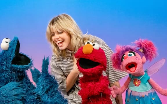 A blonde woman laughs with three puppets.