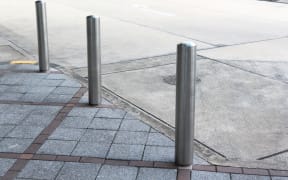 Stainless Steel bollards on grey stone pavement of car park.