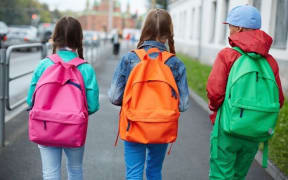 A photo taken from behind of three girls with brightly coloured clothes and backpacks walking down a street.
