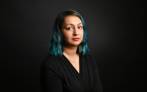 Rona Agrawal, wears black and looks sideways into the camera with a professional but slightly cheeky smile. You can tell that she is proud of herself. Also she has blue hair in this photo.