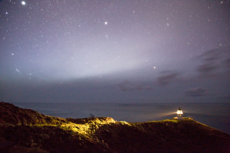 A serene night sky filled with stars above a lighthouse illuminating the coastline, Cape Reinga, New Zealand (Photo by Peter Evans / Connect Images via AFP)