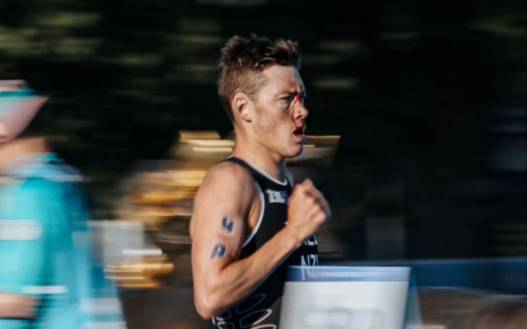 Hayden Wilden runs with blood on his face during the mixed team relay triathlon event at the Paris Olympics. He collided with a French athlete at the start of the cycle leg, dashing the New Zealand team's hopes of a medal.