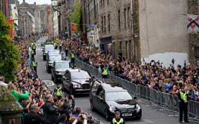 Members of the public stand on Cannongate to watch the hearse carrying the coffin of Queen Elizabeth II, draped in the Royal Standard of Scotland, as it is driven through Edinburgh towards the Palace of Holyroodhouse, on September 11, 2022.