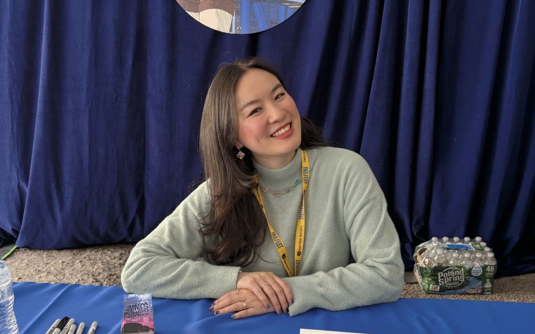 Chloe Gong sits on a table smiling as she gets ready to sign fans' books.