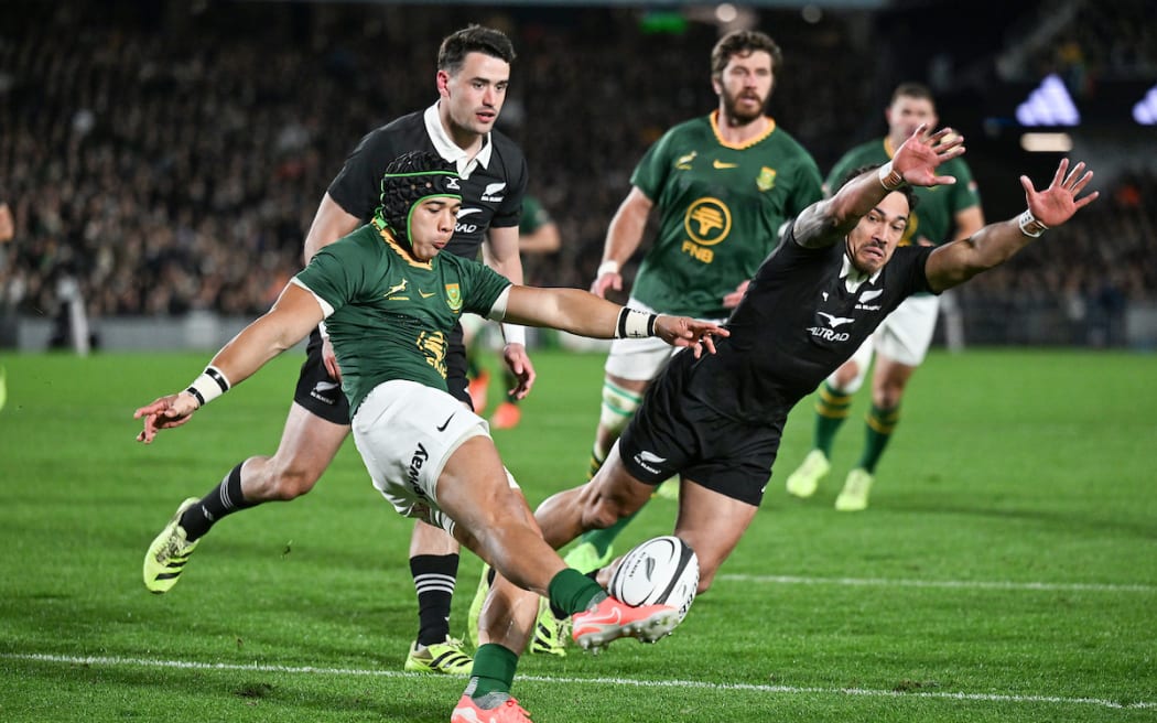 Cheslin Kolbe of South Africa kicks as Billy Proctor of New Zealand dives to block.