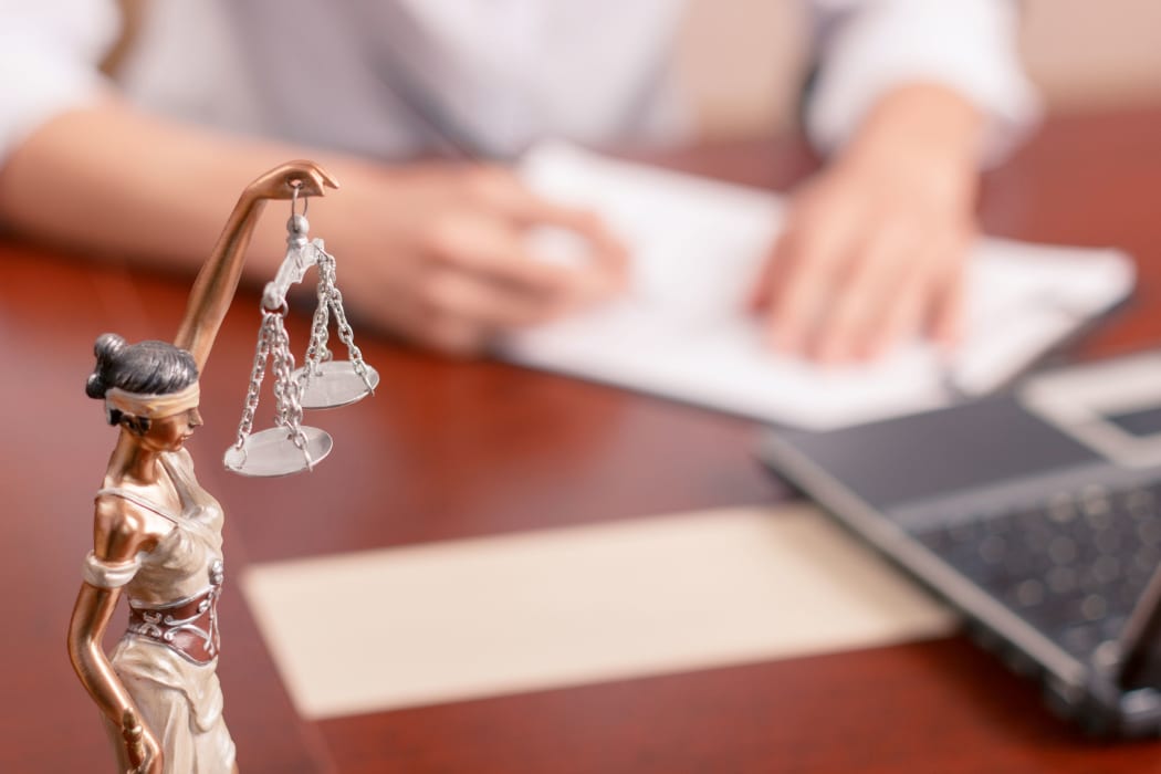 Follow the law. Professional lawyer sitting at the table and signing papers with justice statue standing on surface in forefront.