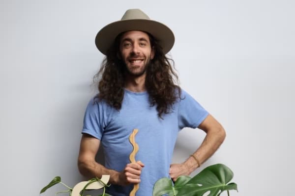 Mike Sullivan is a smiling, long-haired man in a blue t-shirt with plants around him.