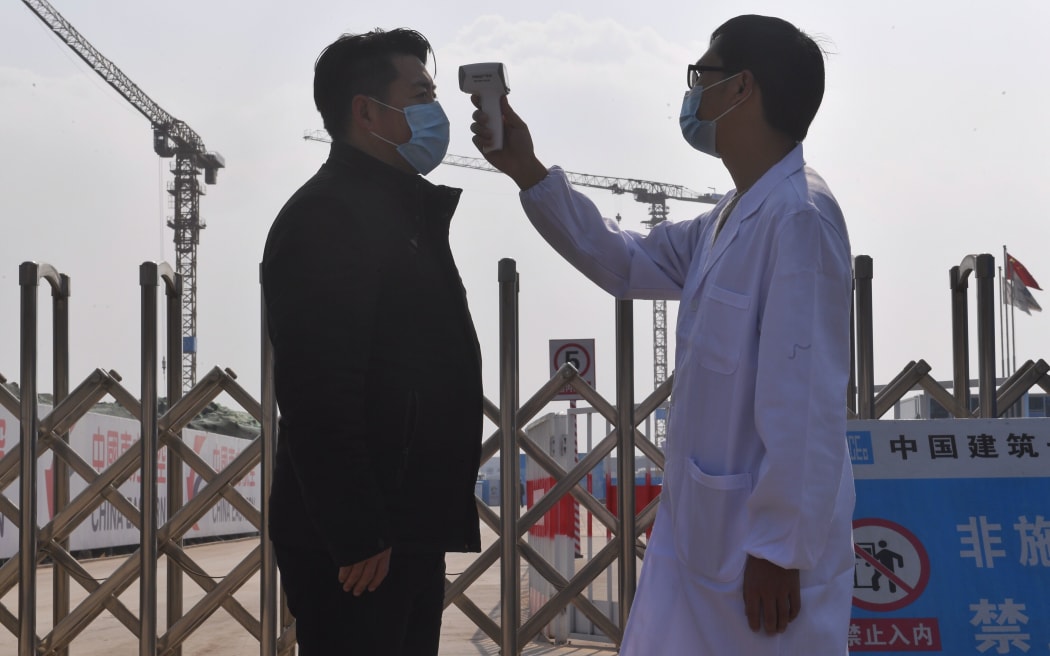 An epidemic prevention staff member checks a person's body temperature before the latter enters the construction site of China Eastern Airlines' production auxiliary area (phase one) in Chengdu Tianfu International Airport, southwest China's Sichuan Province, Feb. 11, 2020.