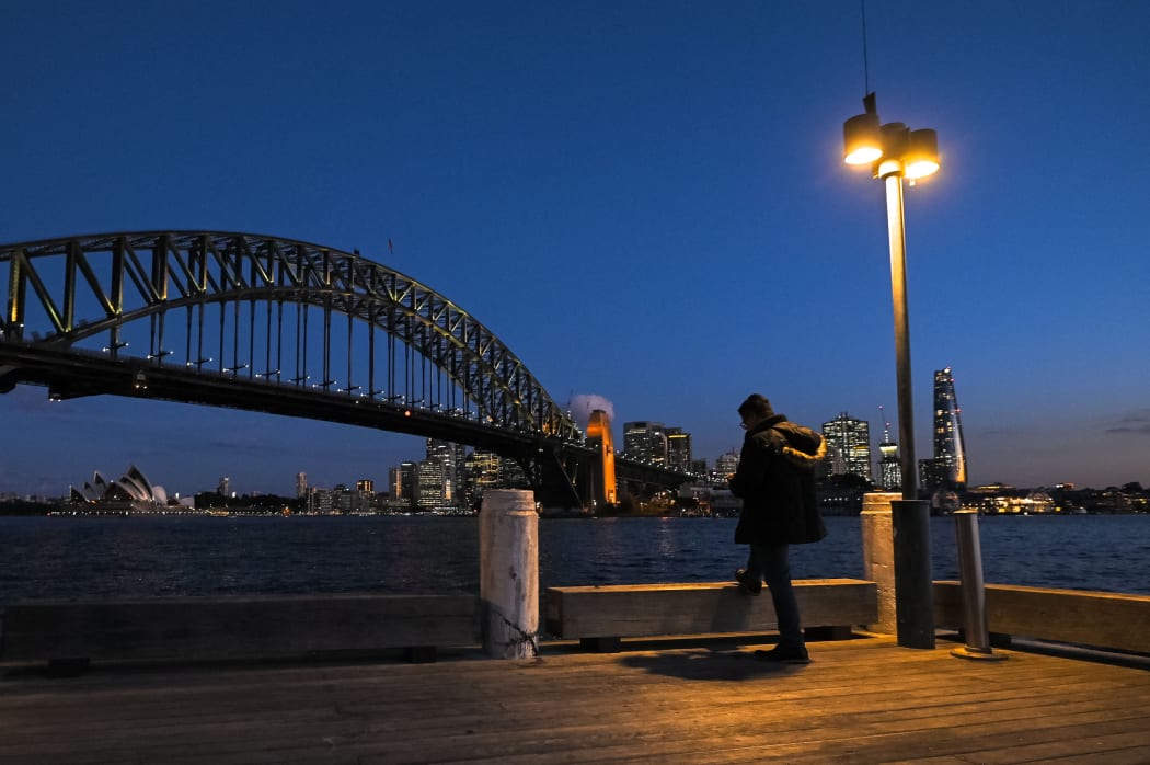 A man stands under a light in front of the Sydney Harbour Bridge at Milson's Point, during lockdown in Sydney.
